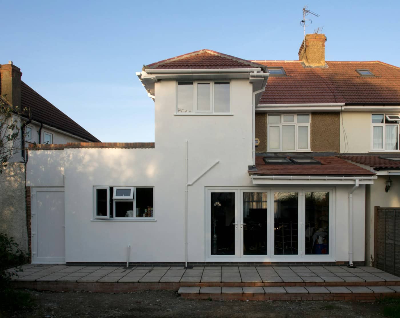 Rear of a semi-detached house with a finished white-rendered two-storey extension, bifold doors and a paved patio.