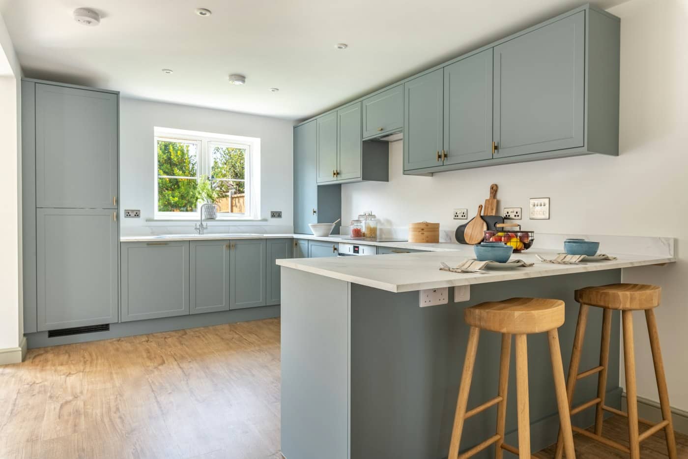 Fitted kitchen with sage-green shaker units, oak worktop breakfast bar and two wooden stools