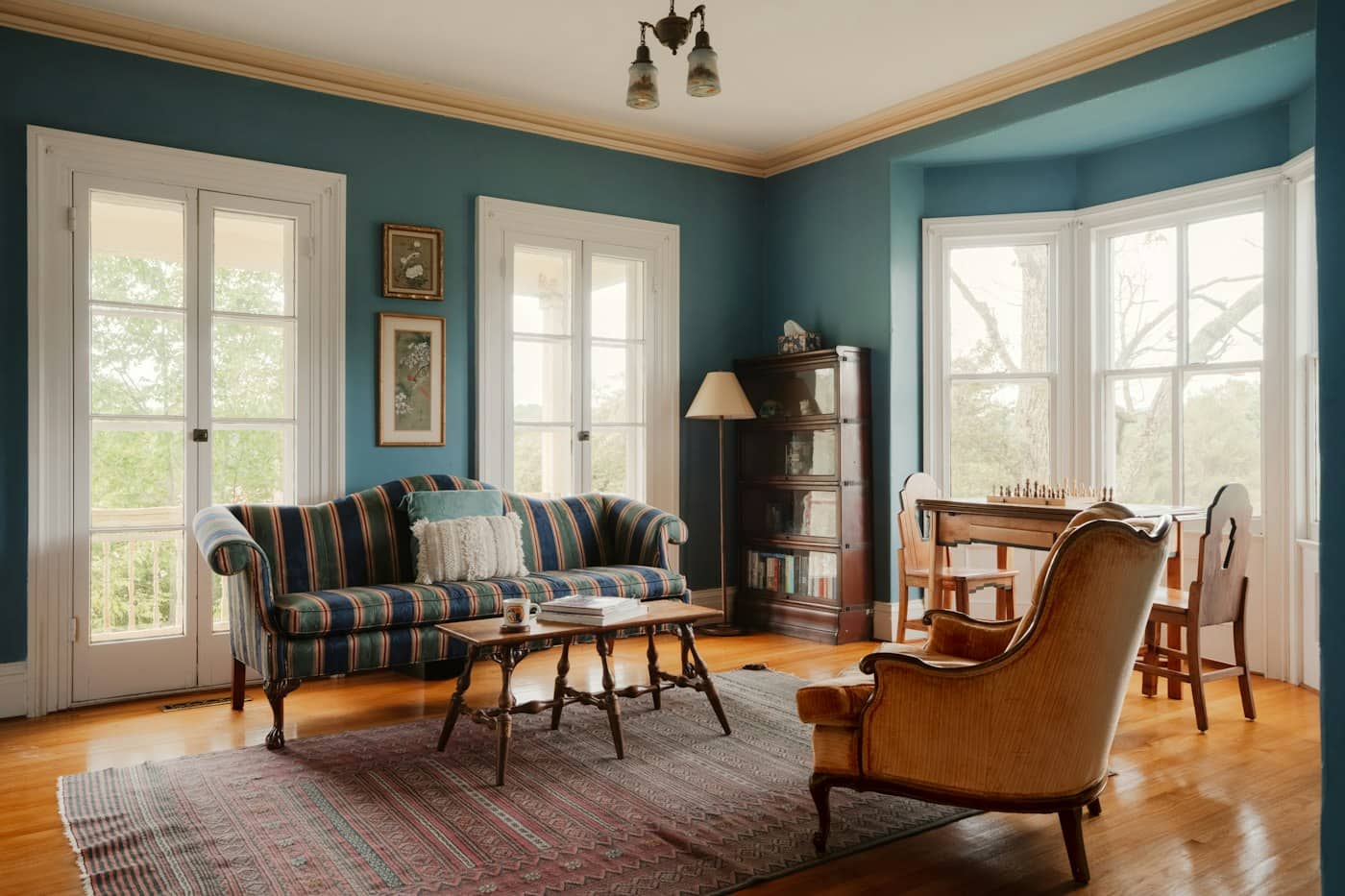 Living room painted teal with white woodwork, cornice, bay window and wooden floor