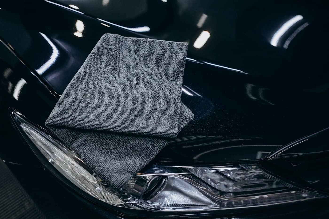 Grey microfibre cloth resting on the gleaming black bonnet of a car beside its headlight